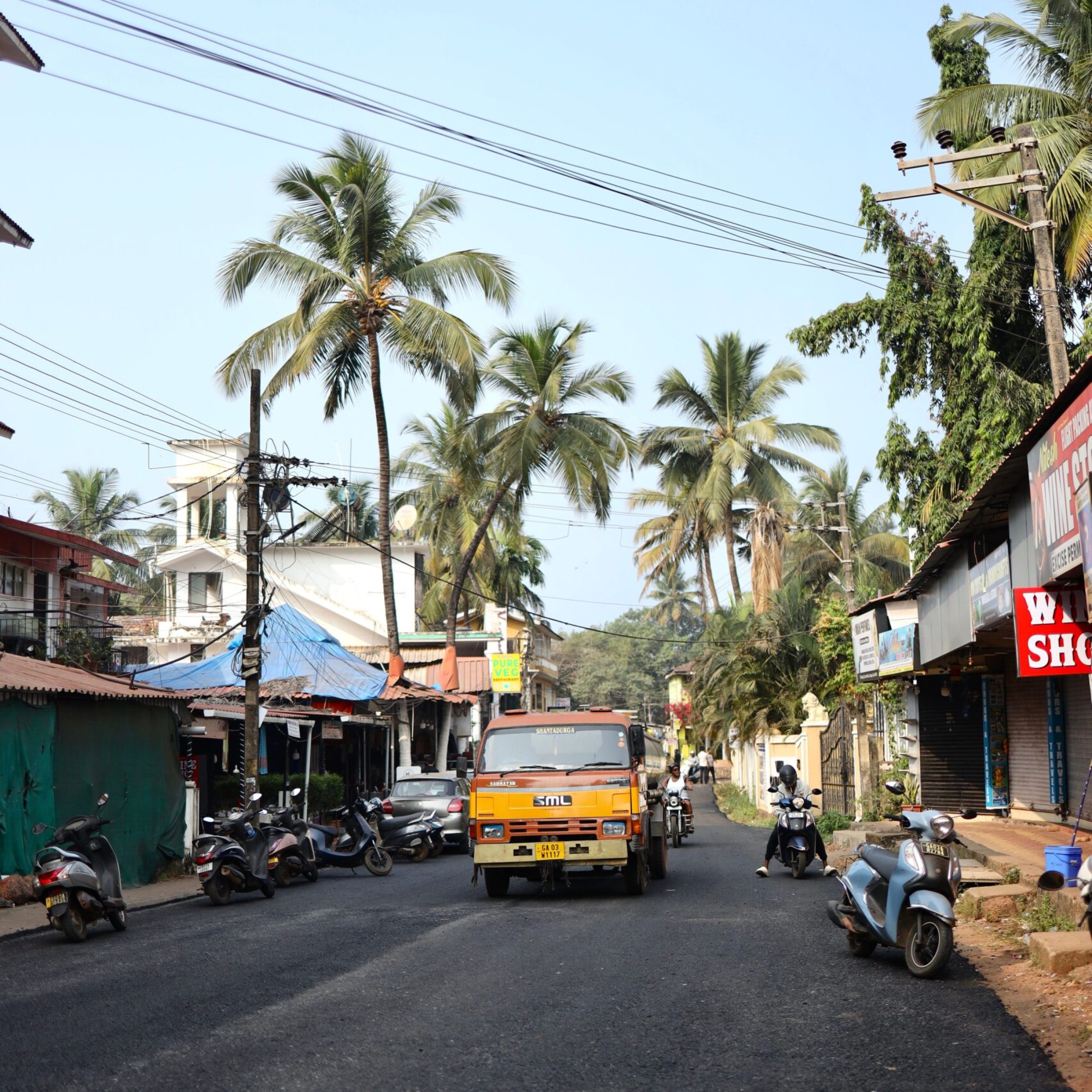 Vibrant street view in Goa, India with palm trees and local shops.